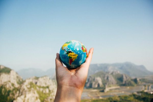 Hand holding up a small globe in front of distant mountains